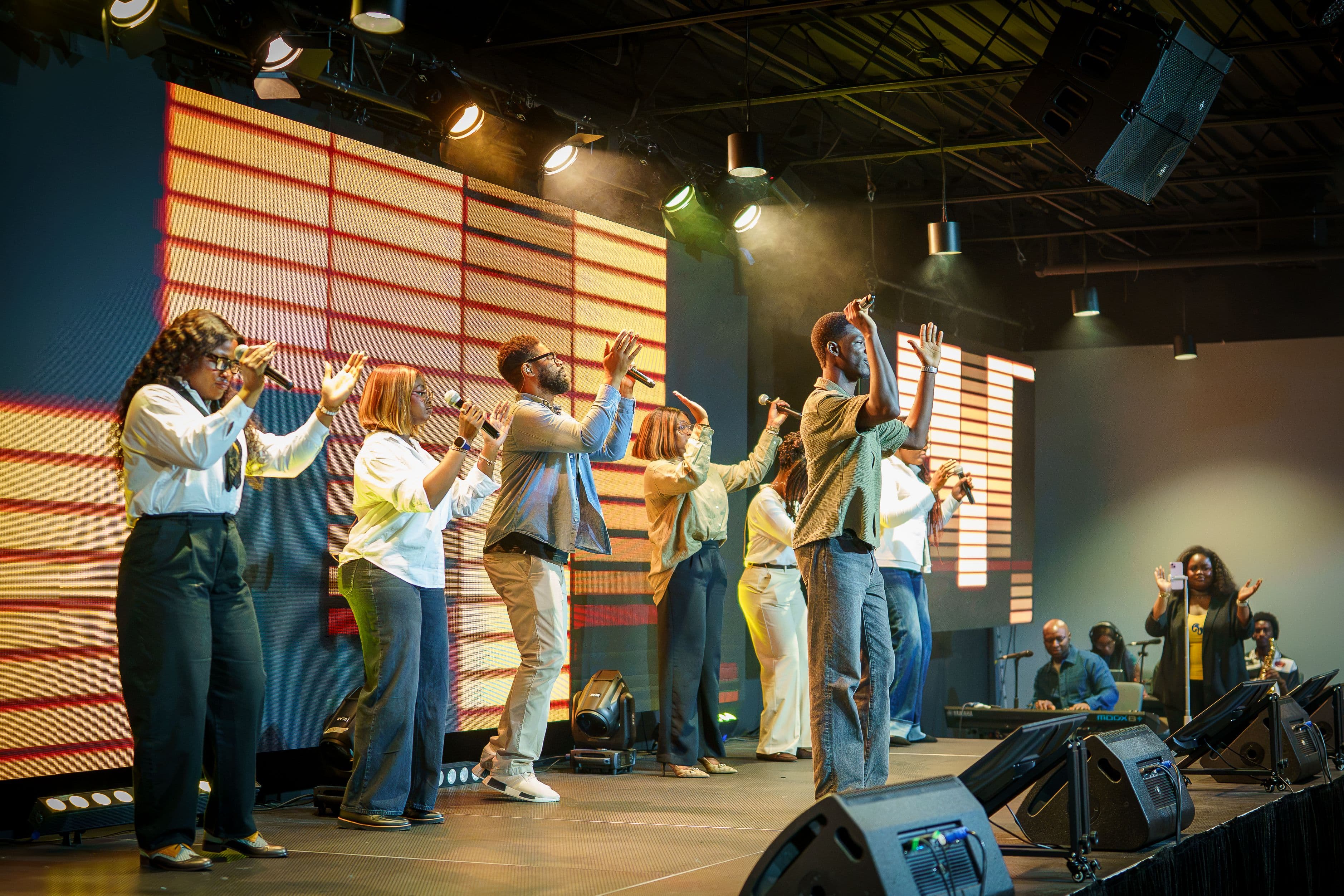 The Lighthouse worship team leading a Sunday service with hands raised, the band behind them and the LED wall lit warm.