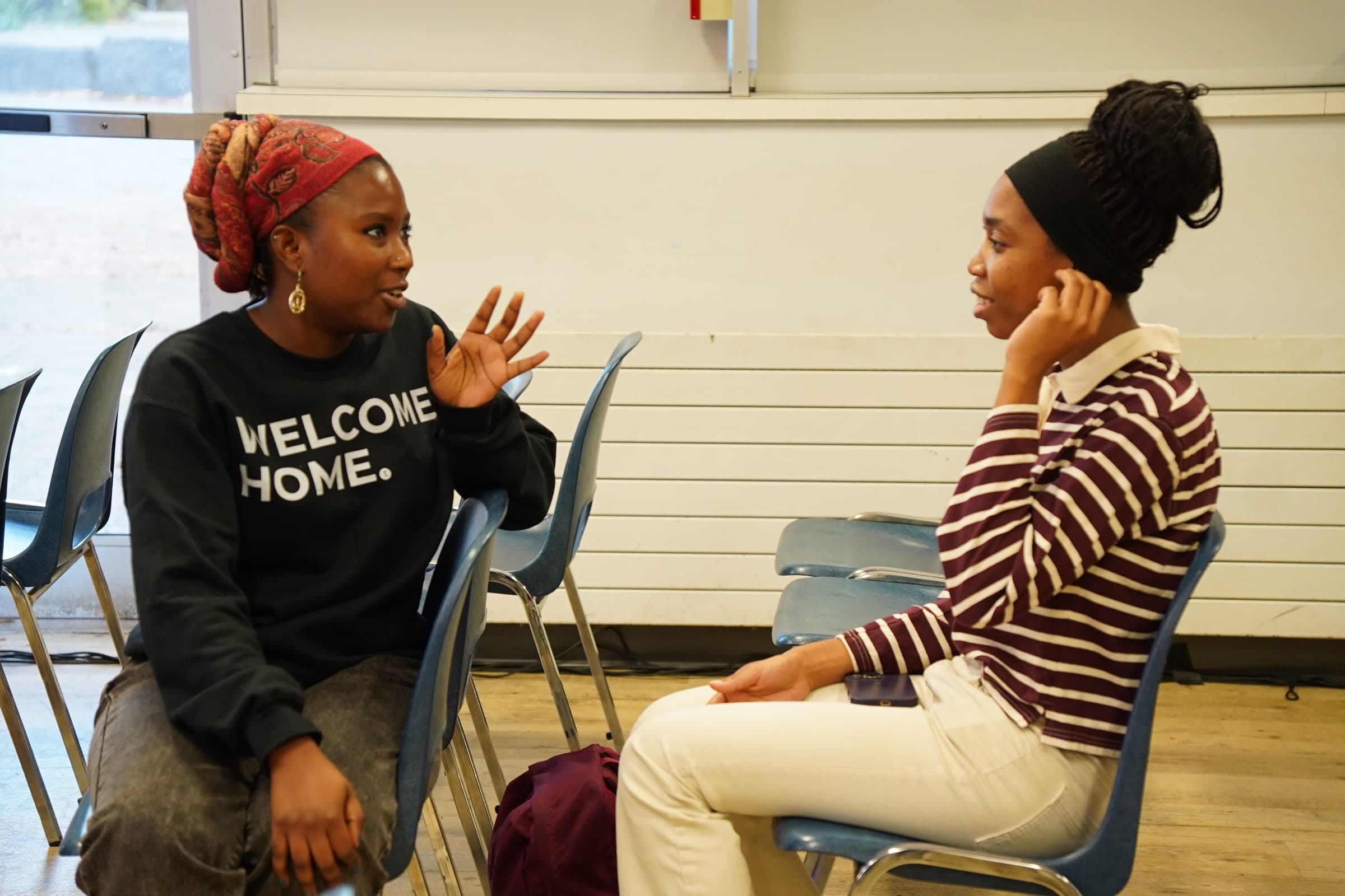 A greeter in a Welcome Home sweatshirt in conversation with a woman seated across from her in the rows of chairs after the service.
